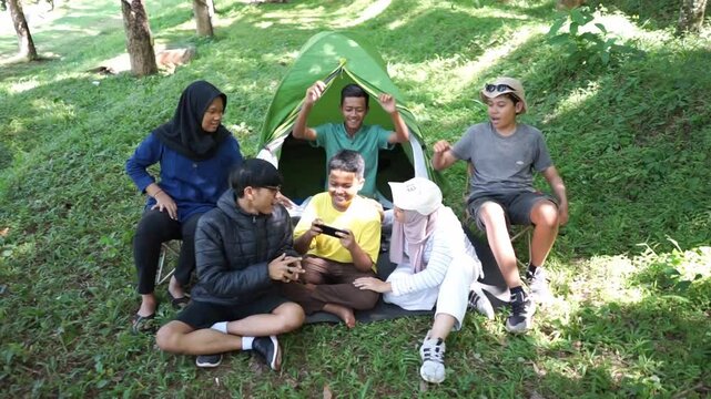 A joyful group of diverse young friends cherishing their bond while camping together in a lush green park on a sunny day.