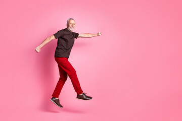 Full size photo of positive senior man dressed brown t-shirt red pants clenching fist fly to empty...