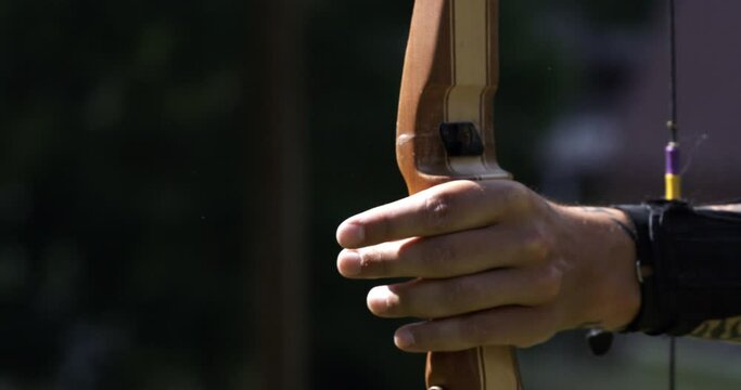 Super slow motion close up of young man with professional equipment is aiming at a target while practising archery with a bow at 1000 fps.