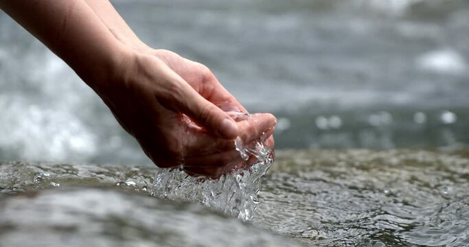Super slow motion close of crystal clear pure water flow stream pouring to woman hand with splashing drops on river lake nature background. Water saving, clean renewable energy and planet preservation