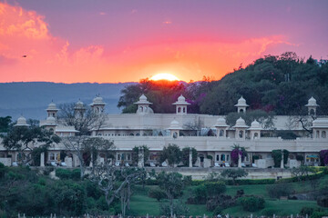 The sun sets behind a large building, painting the dusk sky with colors, Udaipur, Rajasthan, India