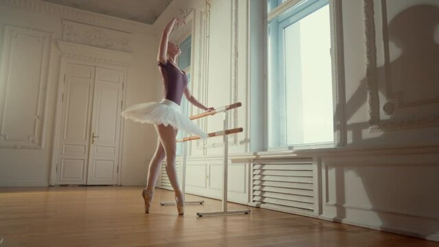 Professional young ballerina in rehearsal room, graceful figure in tutu. Classic music and ballet dance, woman practicing dancing on pointe shoes on parquet, slow motion shot, beauty and art concept