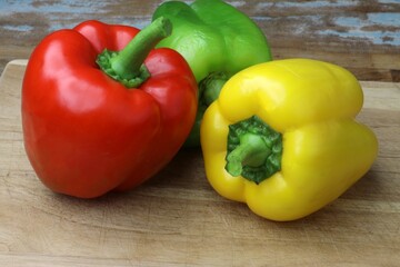 Fresh red, green, and yellow bell peppers on a wooden cutting board