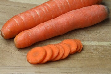 Close-up of two whole carrots and several carrot slices on a wooden cutting board
