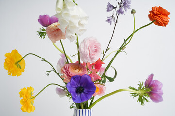 original cheerful composition with a bouquet of mixed fresh colored flowers, ranunculus, anemones, foxglove flower and others on a white background