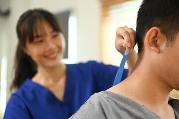 Physiotherapy specialist applying kinesio tape on the shoulders and neck of athlete patient. Sport physical therapy concept