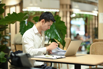 Obraz premium Focused adult businessman working with laptop while sitting in modern office lobby space with plants