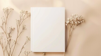 Blank white book mockup on beige background with dry flower flat lay