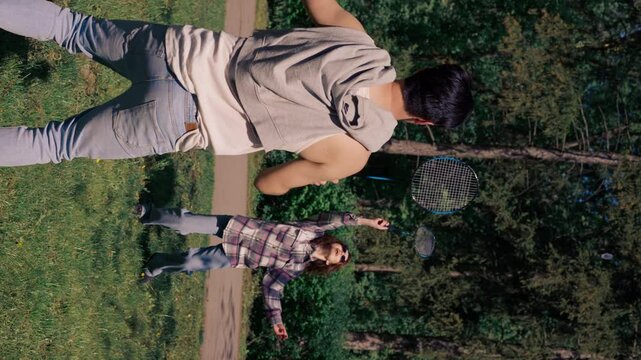vertical video outdoors in a park with trees a young brunette guy with a brunette girl playing bambinton best friends relaxing together the girl serves