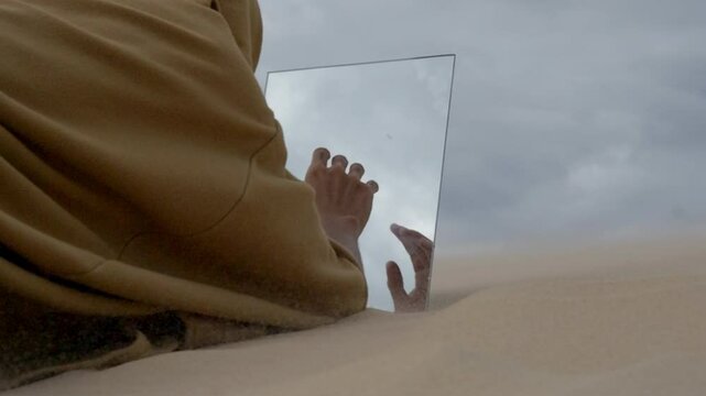 monk in robe finding a mirror in the desert sand dune during a storm and touching his reflection like a mirage