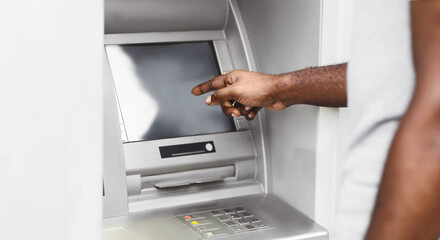 A close-up of a persons hand interacting with an ATM screen. The persons arm and shoulder are...