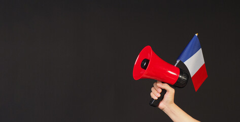Hand is hold french flag and red megaphone on black background
