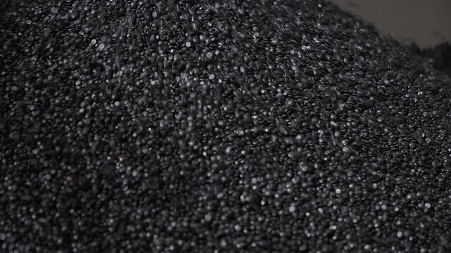 Huge amounts of black plastic material pellets piling up in the container. Piling lots of small recycled plastic pellets. Pouring the repurposed plastic pellets into the pile. Production process.