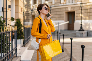 stylish elegant woman on shopping in city street wearing bright colorful yellow suit summer style