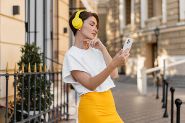 stylish woman wearing yellow headphones listening to music taking pictures on smartphone camera