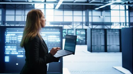 Woman walking in high tech facility, using laptop to patch network issues leading to slow data transfer rates. Employee in data center fixing errors affecting servers performance, camera B - Powered by Adobe