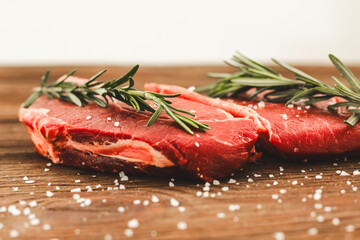 A piece of premium meat, striploin steak on a wooden table with a sprig of rosemary