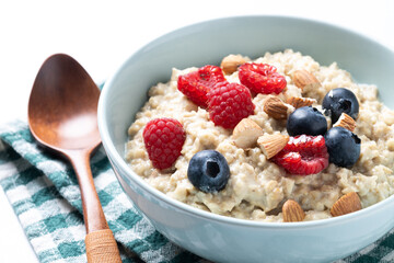 Oatmeal porridge with raspberries, blueberries and almonds in bowl isolated on white background