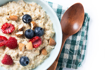 Oatmeal porridge with raspberries, blueberries and almonds in bowl isolated on white background