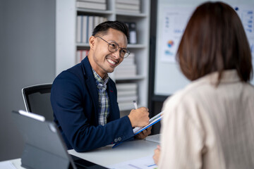 A man and a woman are sitting at a desk with a clipboard in front of the man