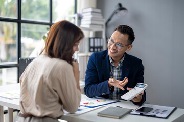 A man and a woman are sitting at a desk with a calculator and a stack of papers