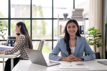 Fototapeta premium A woman in a blue suit sits at a desk with a laptop and a stack of papers