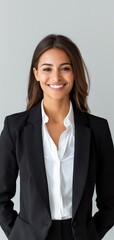 Smiling young businesswoman in a black suit and white shirt, confidently posing in an office environment with a gray background.