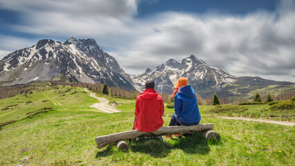 Travelers couple enjoying the mountains, pausing on a bench at viewpoint
