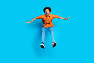 Fototapeta premium Full length photo of impressed positive guy dressed orange shirt jumping high empty space isolated blue color background