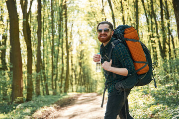 In glasses and with backpack. Bearded man is in the forest at daytime