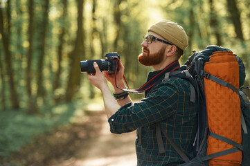 Photographer with camera. Bearded man is in the forest at daytime