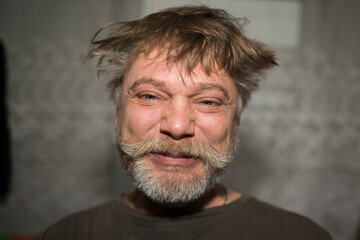 Fototapeta premium The mans messy hair frames his face as he makes a funny expression, showcasing his beard, moustache, and wrinkles. His chin, nose, and jawline add character to his playful smile
