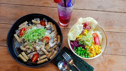 Pasta with mushroom on back plate, vegetables salad and a glass of juice at restaurant table