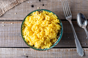 Top view of a bowl with yellow rice with saffron and cutlery.