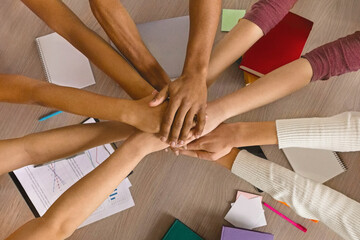 Multiracial teenagers joining hands together in cooperation, preparing common academic project, top...