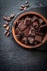 Chocolate chunks in a wooden bowl. Stone counter top. Copy space. Cocoa beans. Top view