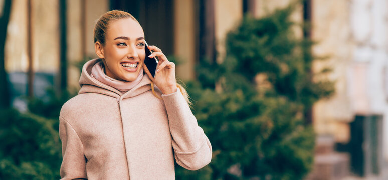 Happy smiling woman talking on cellphone outdoors in city, enoying walk at autumn day