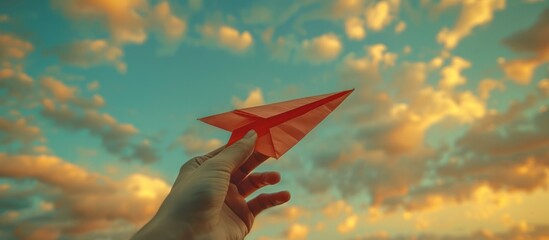 Hand holding a paper airplane against a sky background