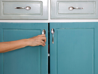 Close-up of gray blue painted kitchen cabinet and woman's hand pulling a handle