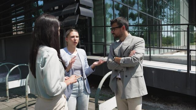 Group of young successful business people, businessman and businesswoman standing out of office building in formal wear, discussing about business. Cool happy expatriate company experts exchange info