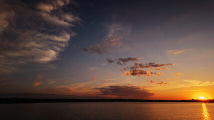 A serene sunset over a tranquil lake with rippled water, sky with soft clouds