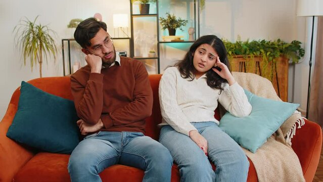 Upset stressed diverse couple sitting on sofa talking discussing at home. Man comforting Indian girlfriend embracing. Trusting relations compassion. Problem, depressed feeling bad annoyed, burnout