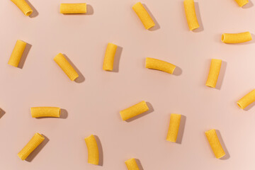 Uncooked rigatoni pasta scattered on a pink background