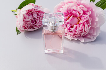 A crystal bottle of women's perfume stands in front of chic pink fresh peonies. presentation of the product, fragrance. Blank bottle mockup.