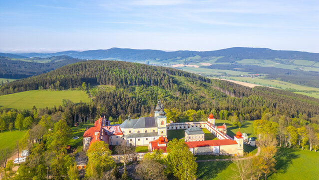 An aerial view of Hora Matky Bozi Monastery, located in Dolni Hedec near Kraliky, Czechia. The monastery is surrounded by lush greenery and a scenic landscape.
