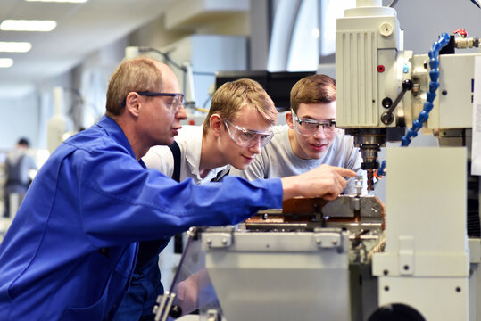 young apprentices in technical vocational training are taught by older trainers on a cnc lathes machine