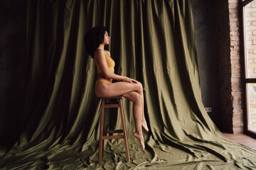 Obraz premium Full body unretouched profile portrait of gorgeous model girl sit chair empty space khaki curtain background