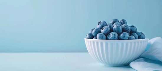 Closeup of blueberries in white porcelain bowl with blue napkin isolated on pastel background. Shallow depth of field. Selective focus. Copy space image. Place for adding text and design