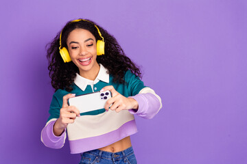 Portrait of lovely young girl play game smart phone wear shirt isolated on purple color background