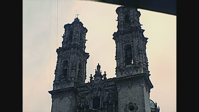 TAXCO DE ALARCON, MEXICO - circa 1970: Mexican peope and vintage cars on the square of the Church of Santa Prisca with bell towers. Archival of Mexico in South America in 1970s.